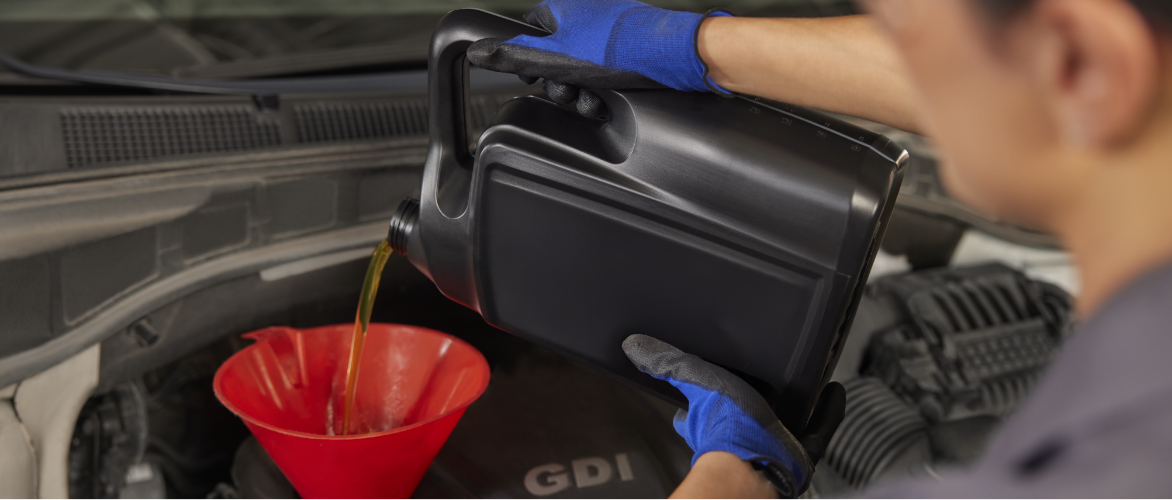 A technician uses a funnel to pour oil into a car’s engine.