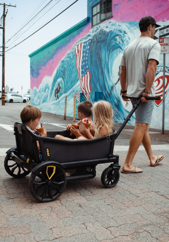 A man pulls three children in a black wagon.