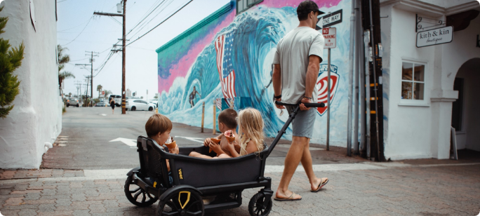 A man pulls three children in a black wagon.