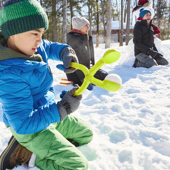 A child uses a green plastic snowball maker outside.