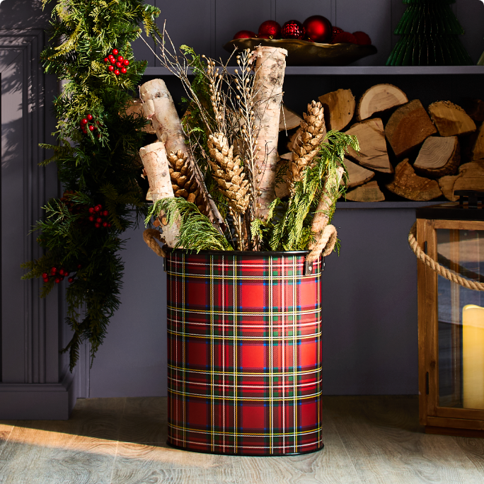 A red plaid container holding birch logs and greenery.