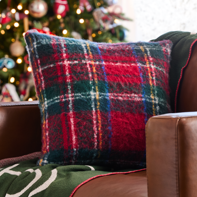 A red and green plaid pillow rests on a brown chair.