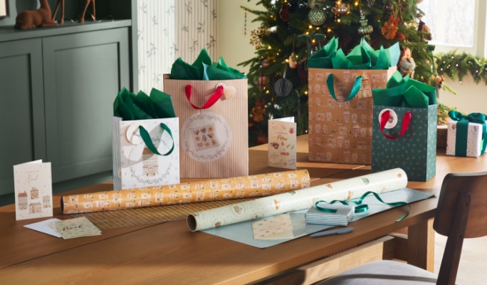 Des rouleaux de papier d’emballage et des cadeaux emballés sous un sapin. 