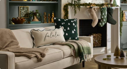 Salon confortable avec canapé, coussins, couvertures, foyer décoré avec des bas et des décorations de Noël sur les étagères.