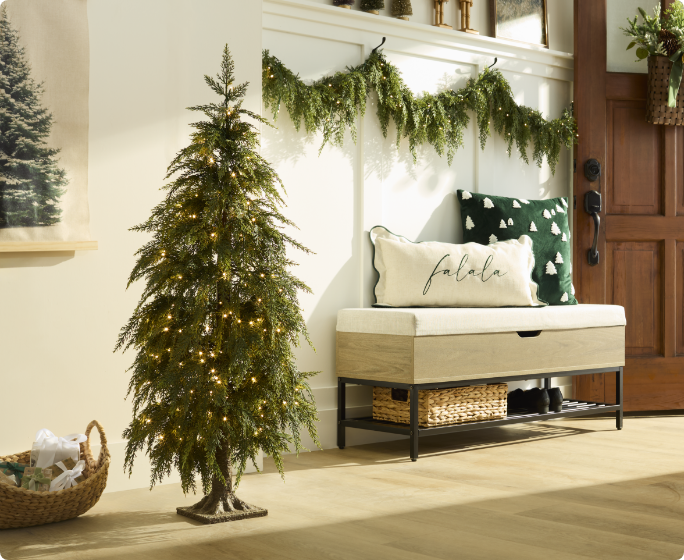 Entrée avec un petit sapin de Noël décoré, un banc rembourré avec des coussins et une guirlande suspendue au-dessus.