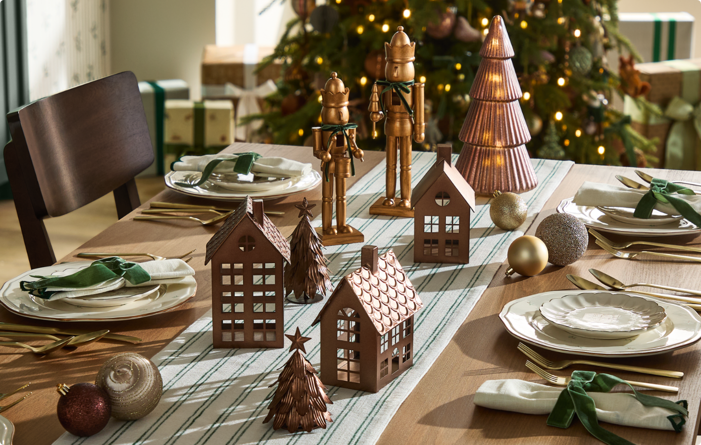 Table à manger festive garnie d'assiettes, de serviettes et de décorations sur le thème de Noël, dont les maisons miniatures et les casse-noisettes.