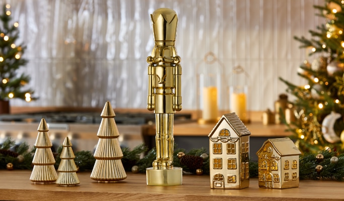 Décorations de table incluant un casse-noisette doré, des arbres dorés et des maisons aux accents dorés avec un arbre de Noël en arrière-plan.
