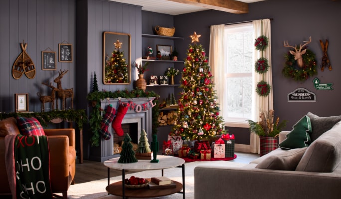 Salon confortable avec un arbre de Noël décoré, un foyer avec des bas de Noël, des décorations murales festives et des meubles décoratifs sur le thème des Fêtes.
