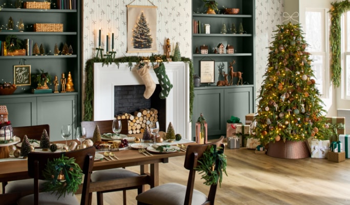Salle à manger festive avec un sapin de Noël décoré, une table à manger dressée et un foyer orné de bas et de guirlandes.