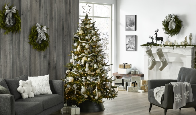 Salon confortable avec un arbre de Noël décoré, des couronnes sur les murs, des bas de Noël sur la cheminée, des coussins et des couvertures festives.