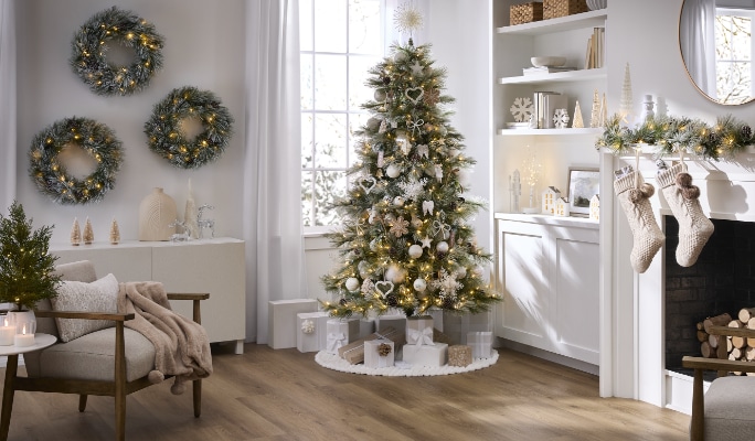 Salon blanc avec un arbre de Noël décoré de décorations blanches, des couronnes sur le mur et des bas de Noël sur la cheminée.