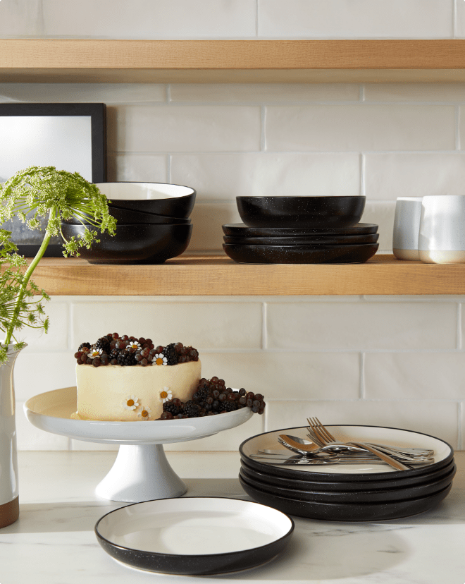 Shelves with black and white dishware, including plates and bowls, next to a cake on a stand.