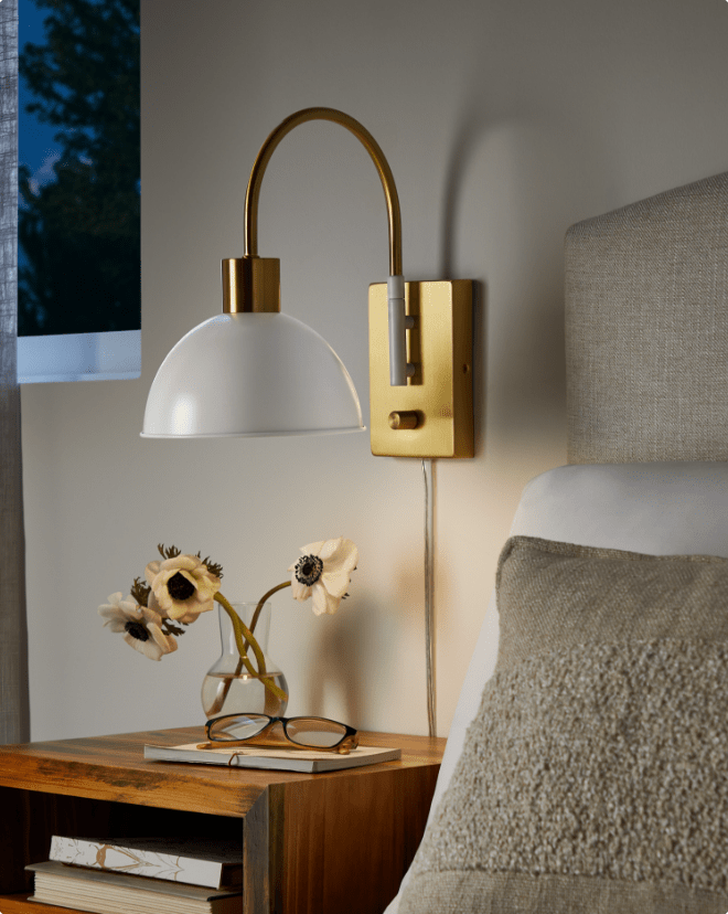 A bedroom nightstand with a decorative lamp and wall-mounted light fixture above it.
