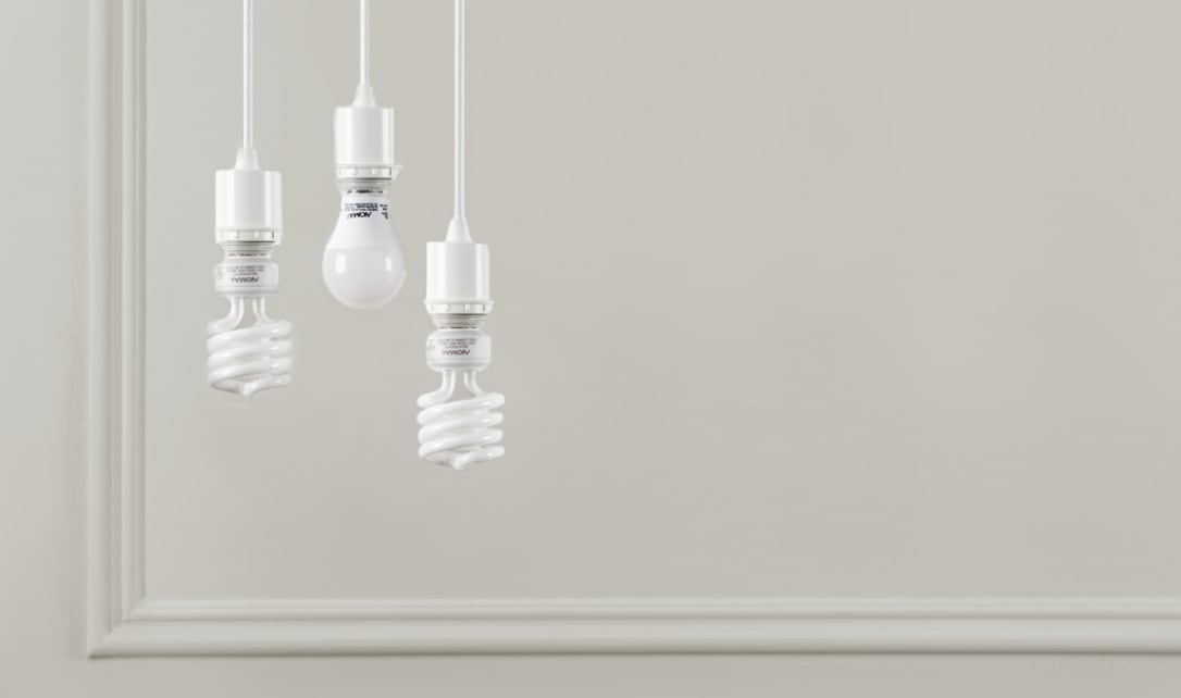 Trois ampoules fluocompactes suspendues fixées de manière minimaliste sur un fond neutre.