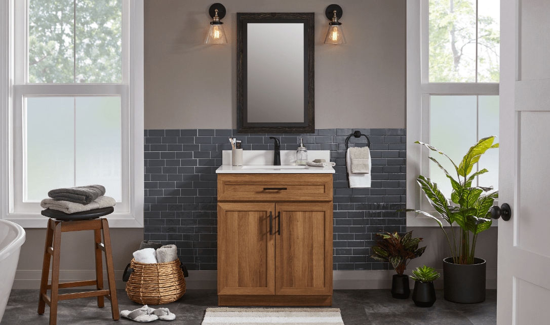 Une salle de bain dotée d'un meuble-lavabo en bois, d'un dosseret noir, d'un miroir rond et de plantes décoratives.