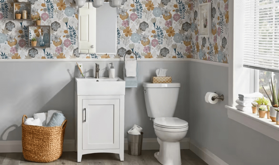 Une salle de bain dotée d'un meuble-lavabo et de toilettes blancs, d'un papier peint floral coloré et de carreaux neutres.