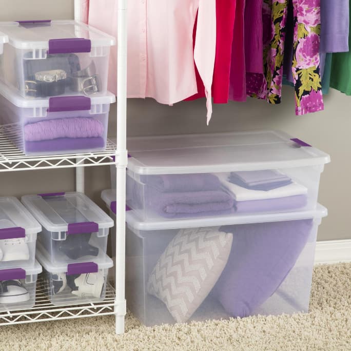 Clear storage bins and boxes containing pillows, towels and other items organized on closet shelves.