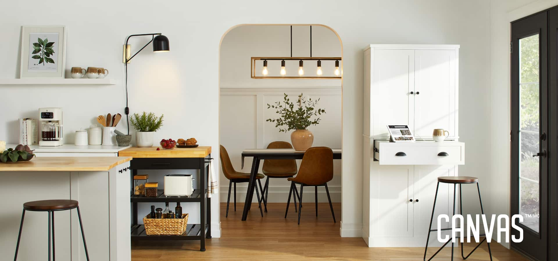 Une cuisine décorée de divers meubles de cuisine CANVAS, d’éclairage et d’accessoires, à côté d’une ouverture regardant dans une salle à manger avec une table à manger et des chaises.