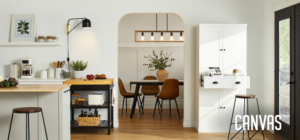 A kitchen dressed with various CANVAS kitchen furniture, lighting and accessories, next to an opening looking into a dining room with a dining table and chairs.