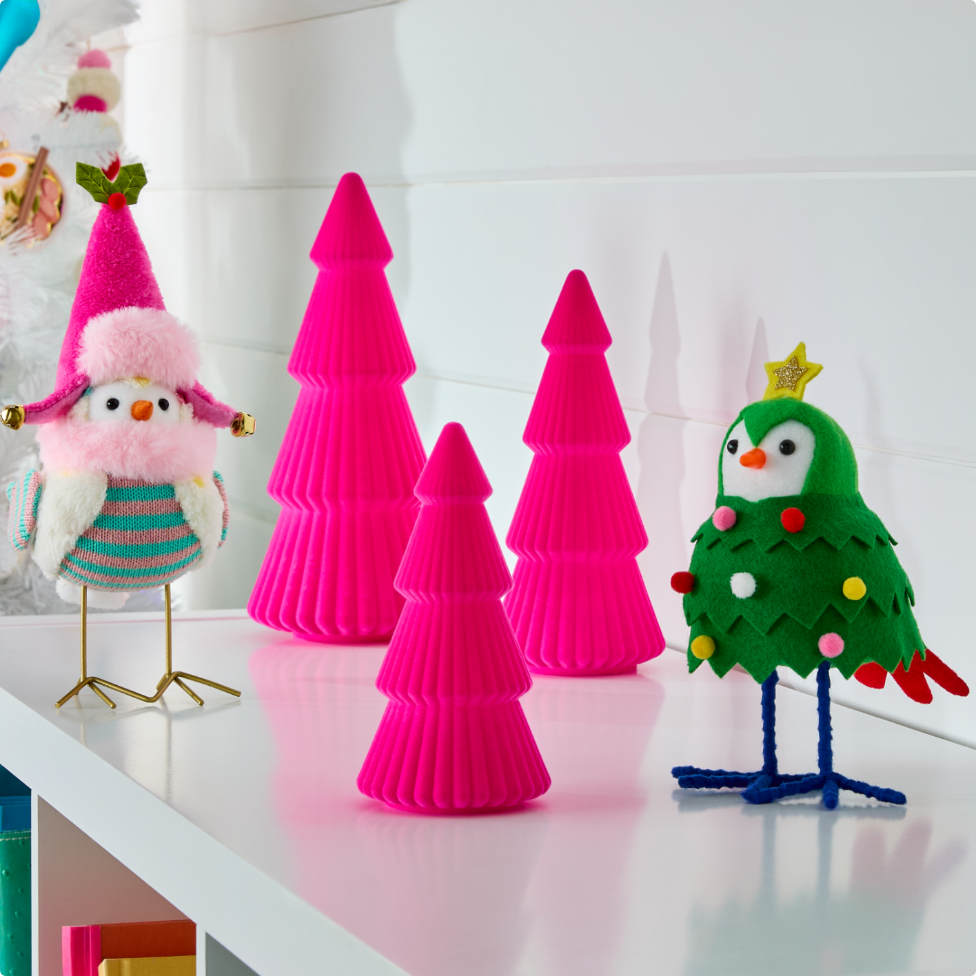 Deux oiseaux décoratifs et trois arbres roses en forme de cône sont exposés sur une étagère. 