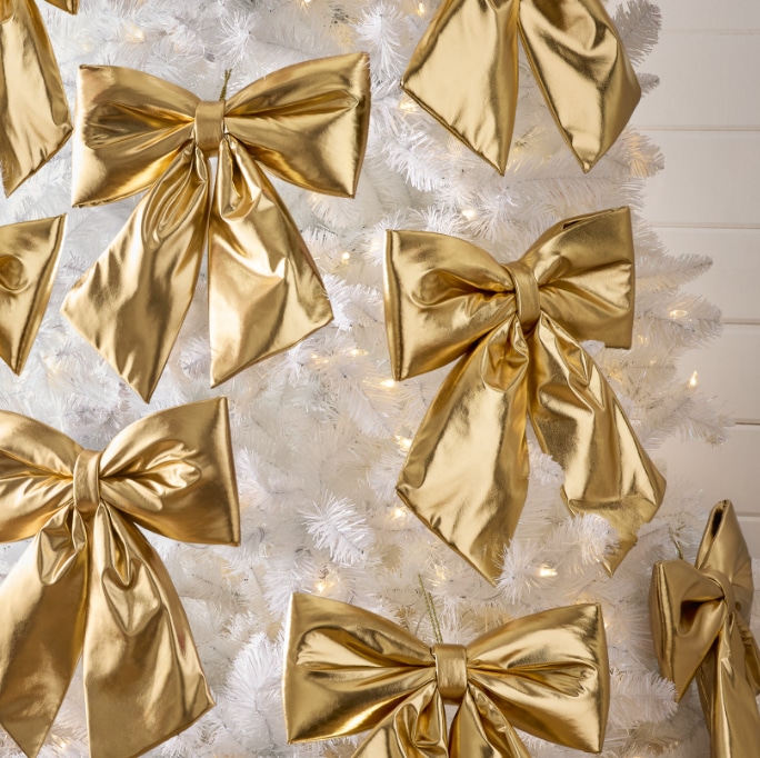 Gros plan sur un sapin de Noël blanc décoré de grands nœuds dorés brillants.