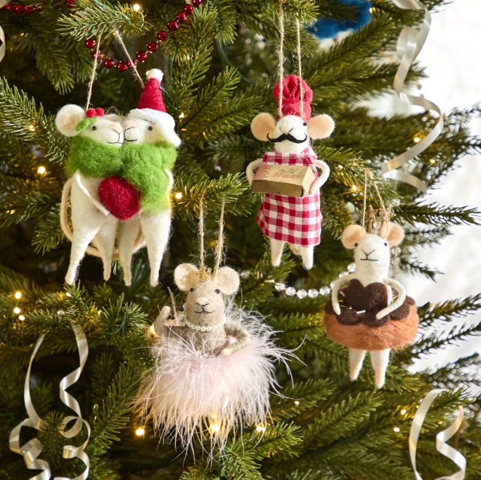 Quatre souris en feutre vêtues de costumes différents sont suspendues à un sapin de Noël.