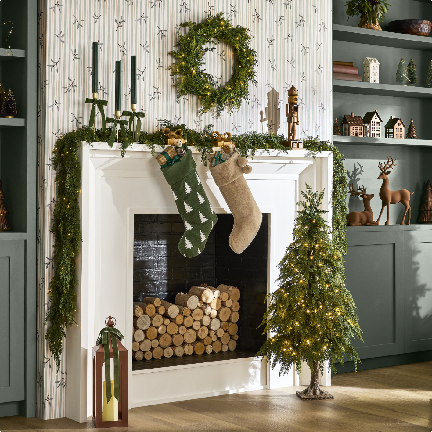 Fireplace decorated with two giant stockings, a wreath and a garland with a small decorated Christmas tree nearby.