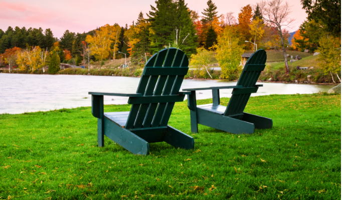 Two Adirondack chairs on a well-kept lawn by a lakeside in Canada.