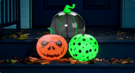 Three inflatable pumpkins with different designs, including a jack-o'-lantern and polka dots, displayed on a porch.