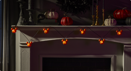 A string of Mickey Mouse pumpkin lights decorating a mantel with assorted pumpkins.