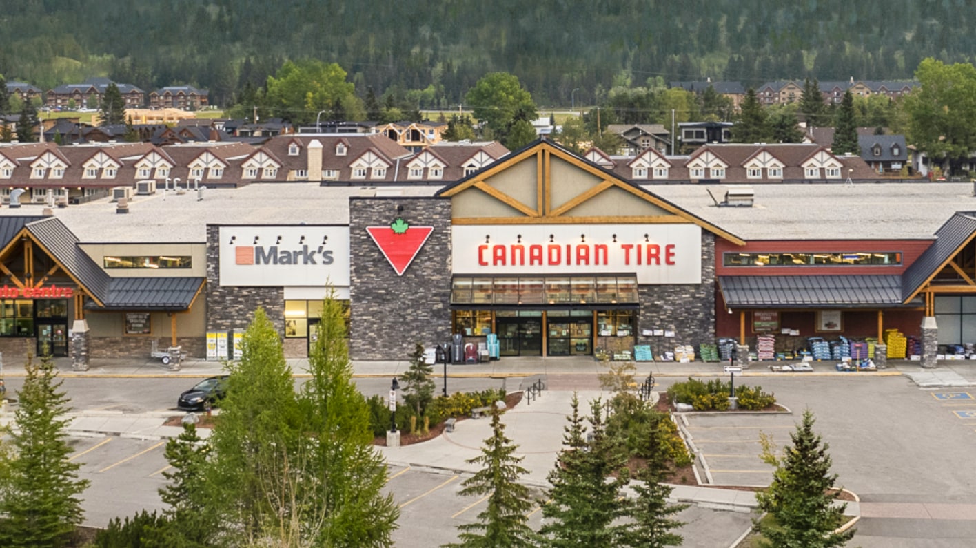 A Canadian Tire store with a Mark's store next to it, set against a backdrop of trees and residential buildings.
