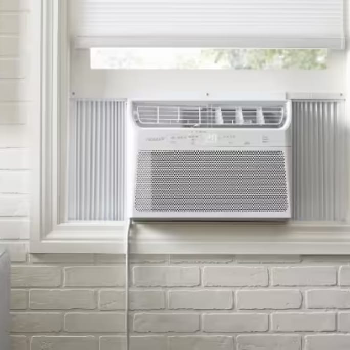 A window air conditioner unit installed in a white-framed window with brick walls surrounding it.