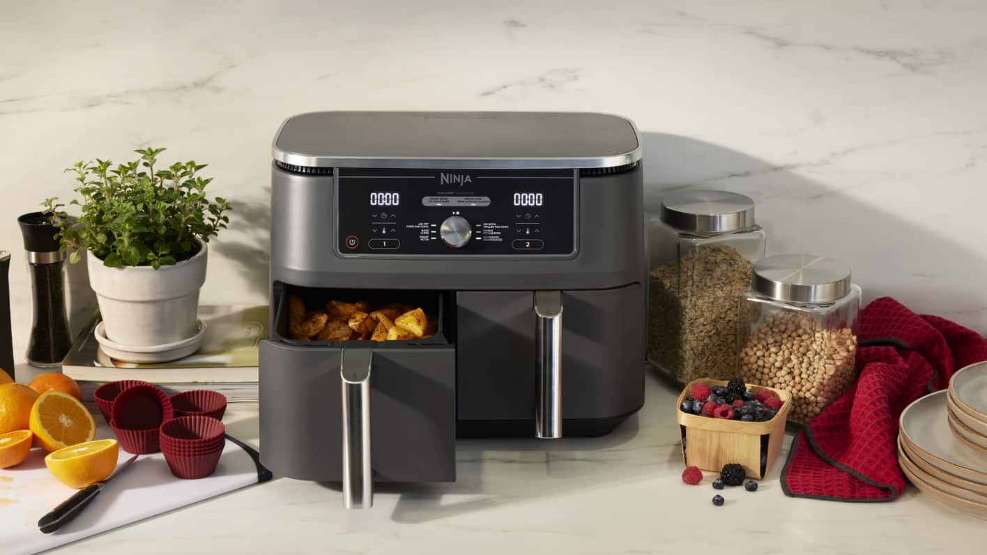 Une friteuse à air Ninja sur un comptoir de cuisine avec divers aliments et ingrédients autour.