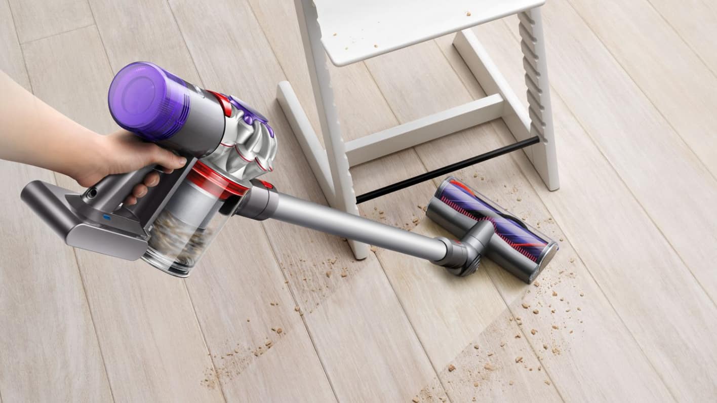 Une personne utilisant un aspirateur balai sans fil pour nettoyer les débris sur un plancher de couleur claire.
