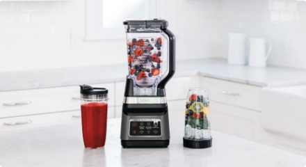 Un mélangeur et une centrifugeuse sur un comptoir de cuisine avec des fruits et des légumes.