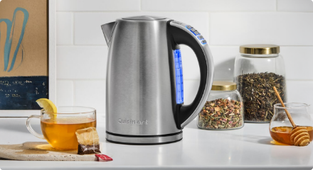 Une bouilloire électrique sur un comptoir de cuisine avec des tasses à thé et d’autres articles essentiels pour la préparation du thé.