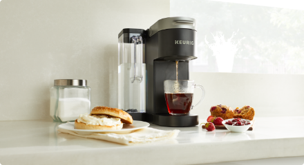Une cafetière sur un comptoir de cuisine avec une tasse de café et quelques ingrédients à proximité.