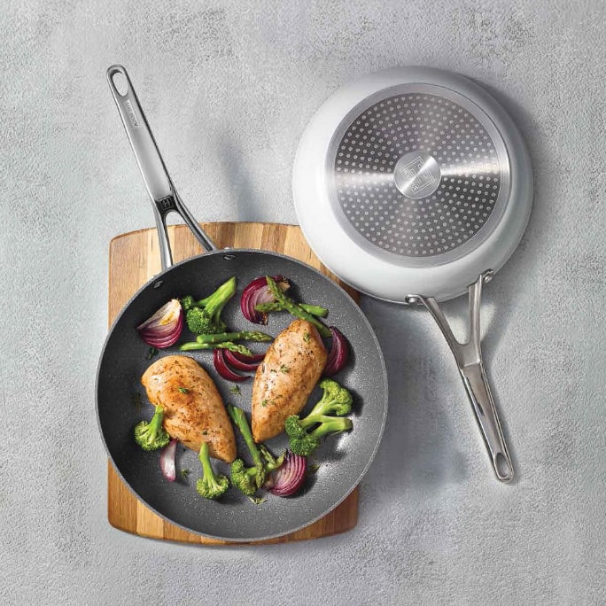 Two frying pans with cooked food and utensils.