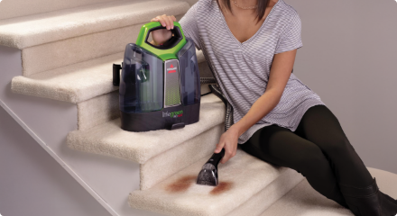 Woman using a carpet cleaner on carpeted stairs.