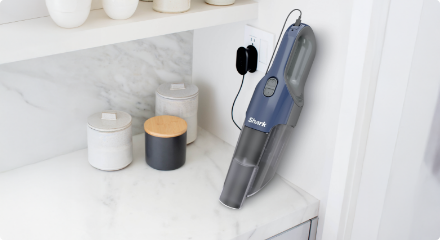 Hand vacuum placed on a white surface next to cleaning supplies.