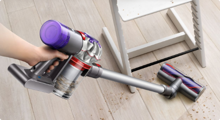 Hand seen using a stick vacuum on a wooden floor.