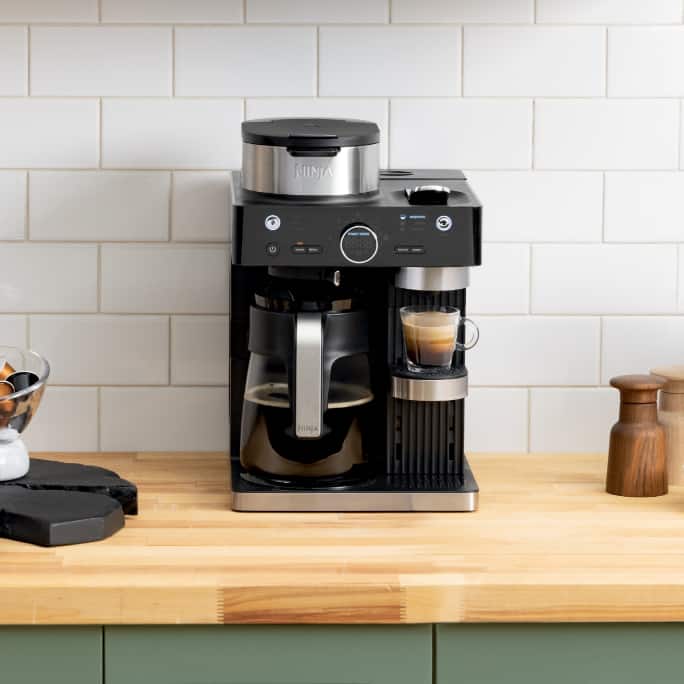 Drip coffee maker on a wooden kitchen counter with a cup of coffee.