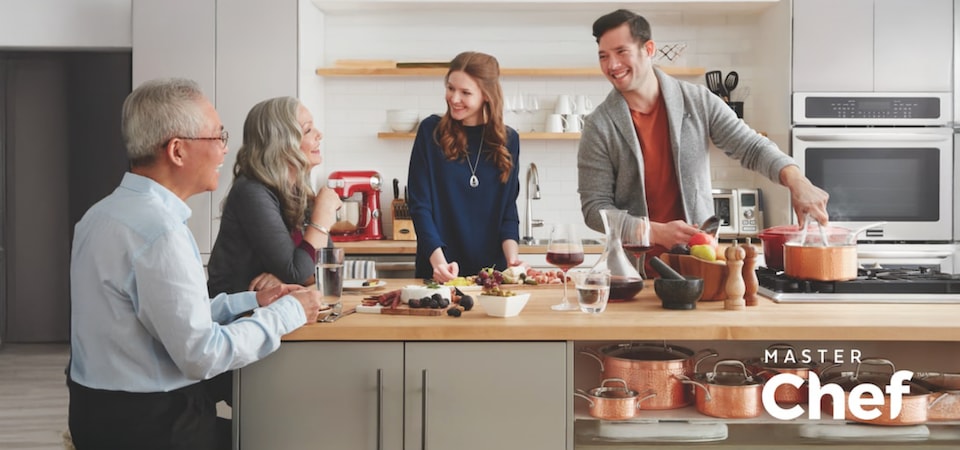 A group of 4 people cooking and eating around a kitchen island.