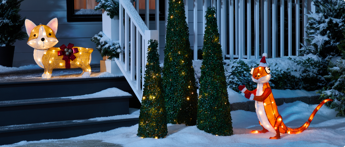 A CANVAS Gigi the Gecko decoration and a CANVAS Georgie the Corgi decoration displayed in a snowy front lawn at night.