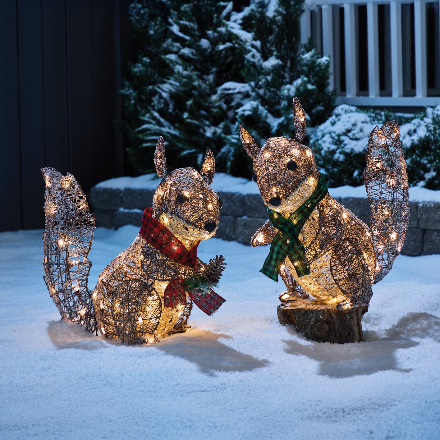 Two light-up squirrel decorations wearing red and green scarves in a snowy yard.