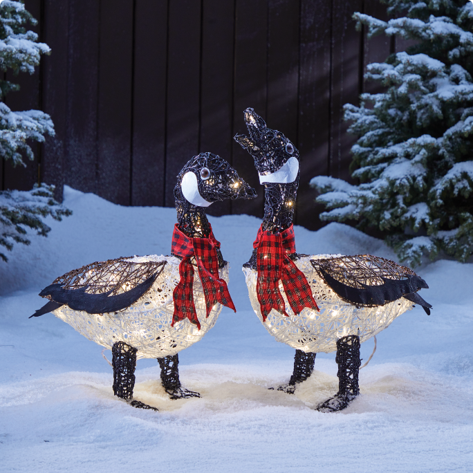 Two light-up geese with red scarves in a snow-covered yard. 