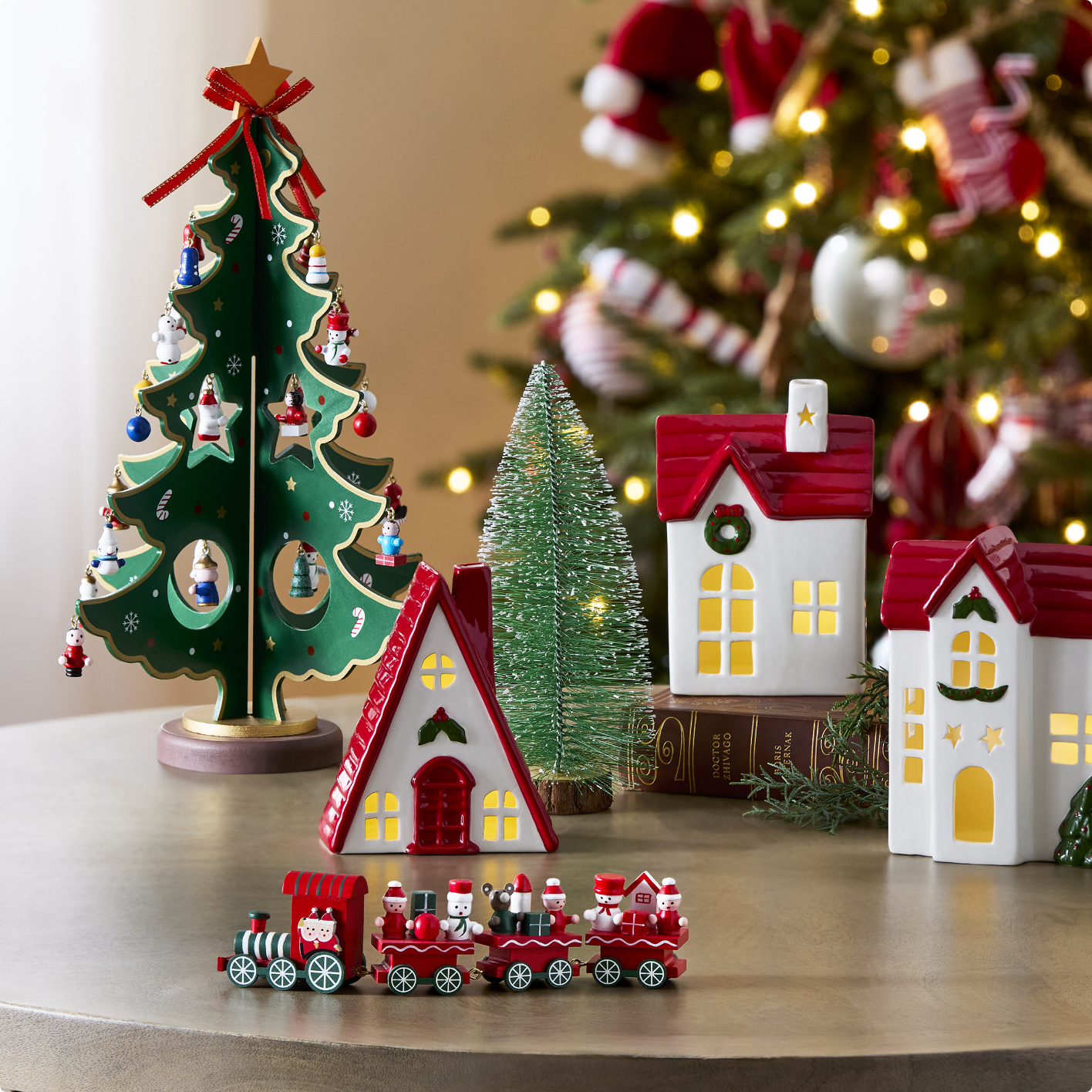 A festive tabletop scene with miniature houses, a Christmas tree decoration, and a small toy train on a table.