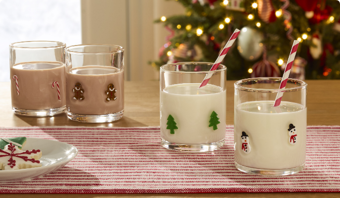 Four festive glasses of milk featuring different patterns: candy canes, gingerbread cookies, Christmas trees and snowmen