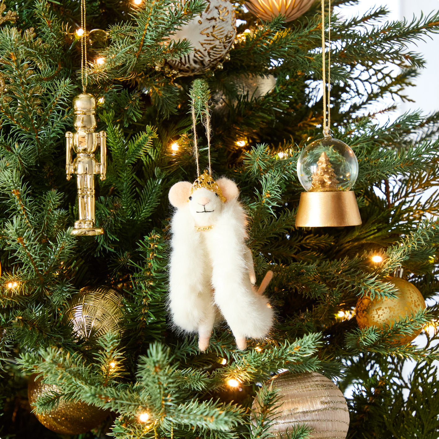 Gros plan sur un sapin de Noël garni d'ornements dorés, dont un casse-noisette, une figurine de souris et une boule à neige.