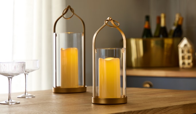 Deux bougies allumées dans des bougeoirs en verre posés sur une surface en bois.